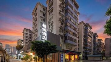 Un edificio de hotel de varios pisos con un letrero llamativo, un acceso cubierto y una calle mojada que refleja las luces del edificio.