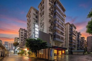 Un immeuble hôtelier à plusieurs étages, avec une enseigne bien visible, une entrée abritée et une rue mouillée qui reflète les lumières du bâtiment.