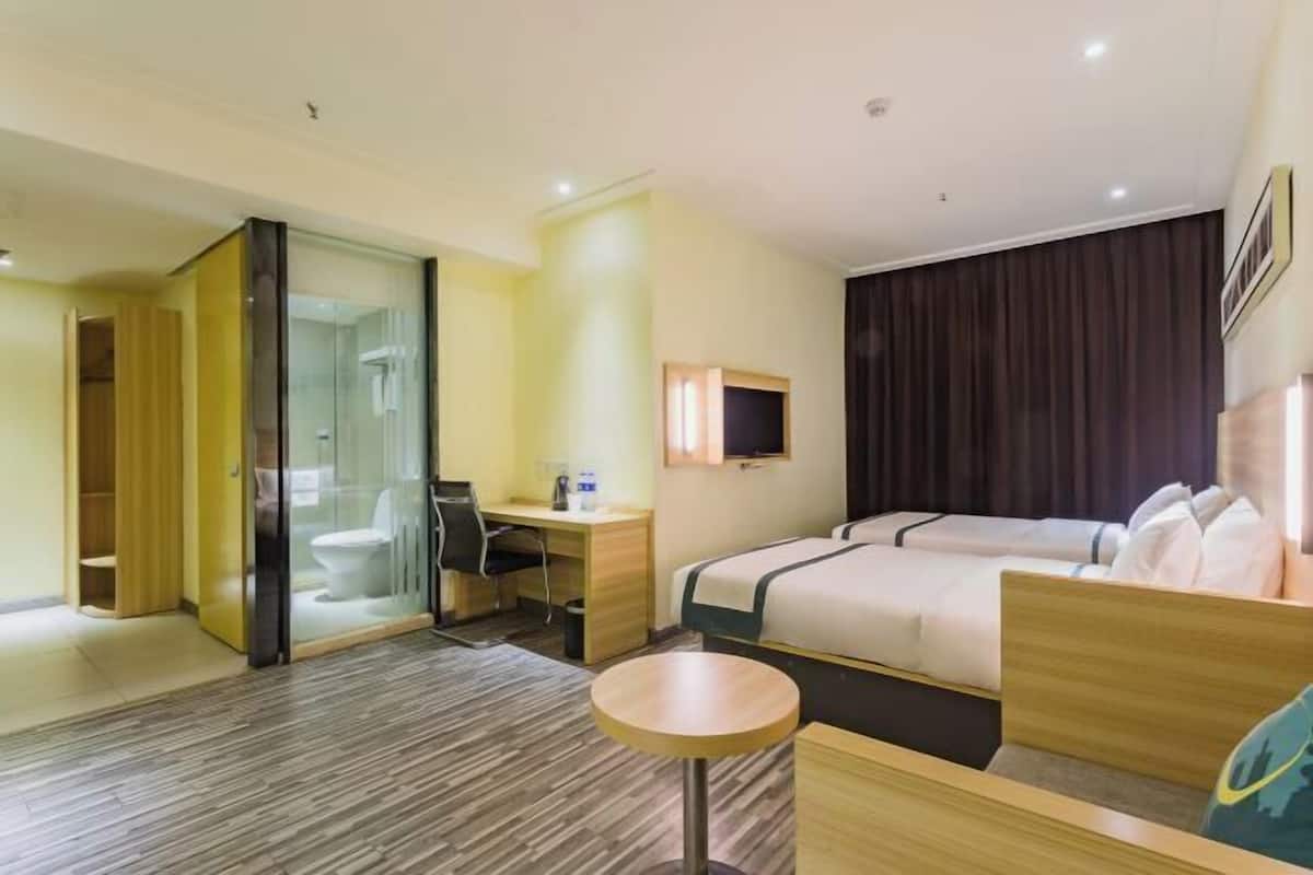 A hotel room with a bed, a desk, a chair, a small round table, a TV, and a sliding door leading to a bathroom.