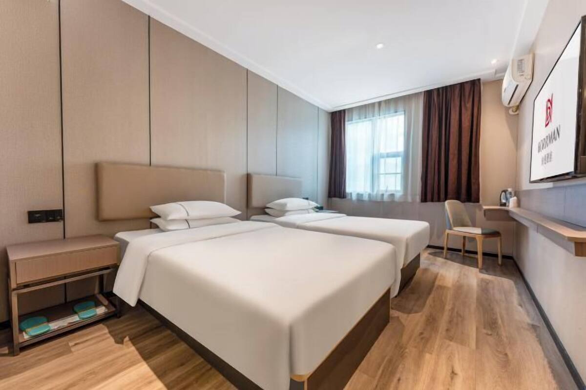 Ein Hotelzimmer mit zwei Betten, einem Schreibtisch, einem Stuhl und einem Fernseher.
