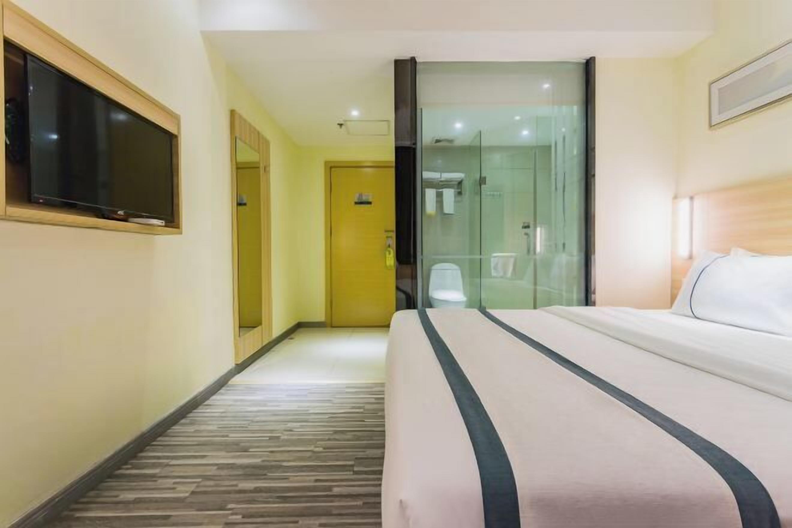 Ein Hotelzimmer mit Bett, Wand-Fernseher, Duschkabine aus Glas und Holzboden.