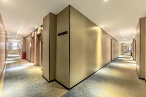 A hotel corridor with a patterned carpet, a red trash bin, and a sign on the wall. - Bohan Hotel (Guangzhou Financial City – Tangxia Metro Station Branch) (Guangzhou)