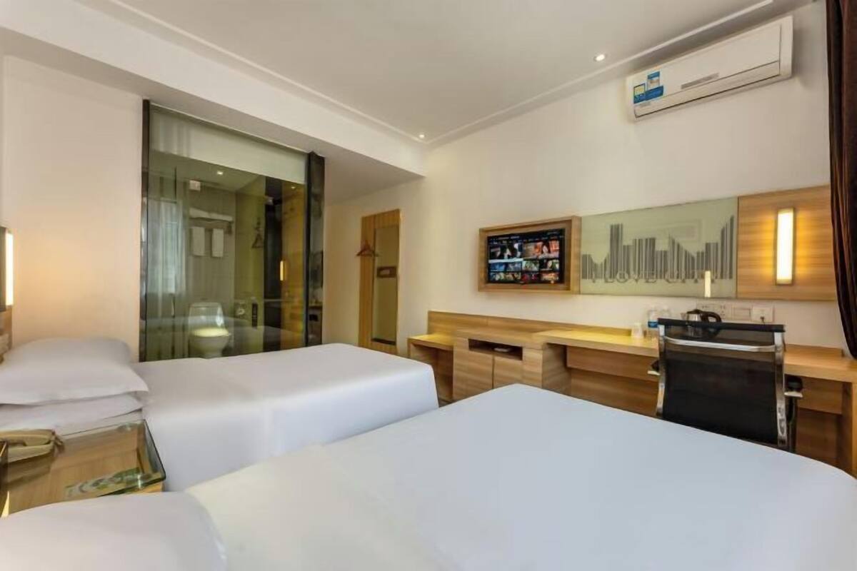 Ein Hotelzimmer mit zwei Betten, einem Schreibtisch, einem Sessel, einem Fernseher und einem Stadtbild an der Wand.