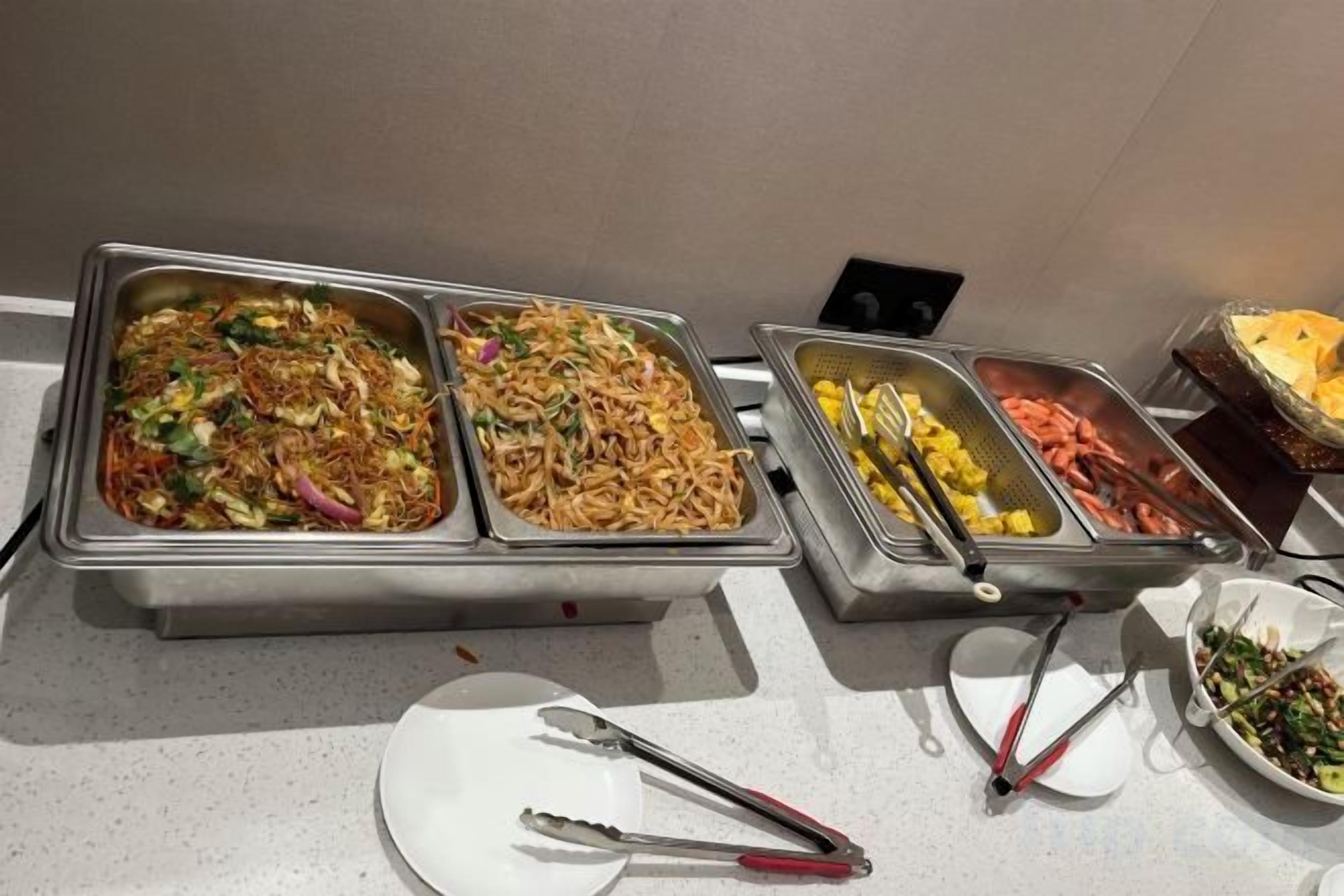 Un bufé con varias estaciones de comida, incluyendo fideos, mariscos y ensaladas.