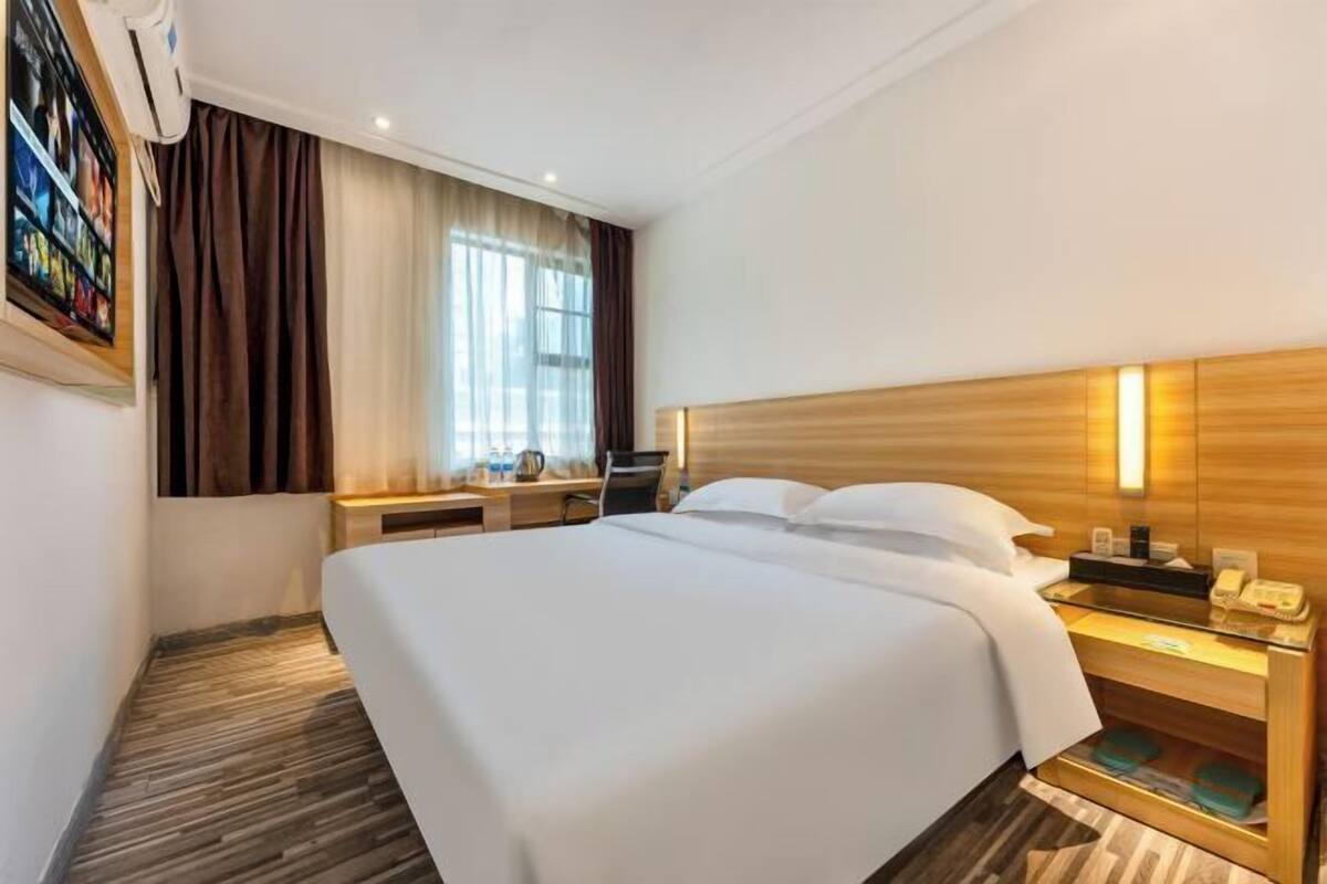 Ein Hotelzimmer mit einem großen Bett, Nachttischen, einem Schreibtisch und einem Fenster mit Vorhängen.