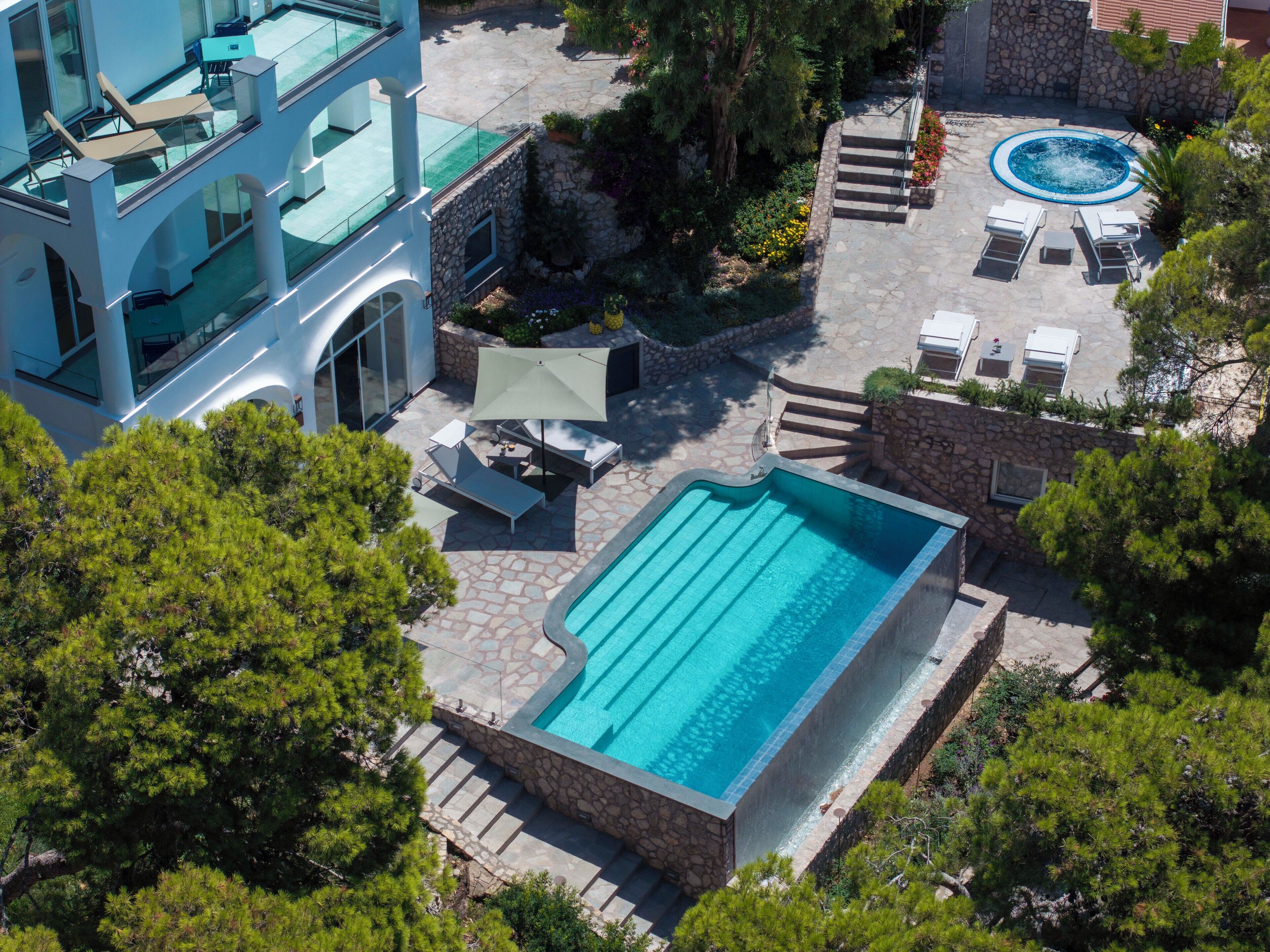 A rooftop pool with a stone deck, lounge chairs, and a hot tub.