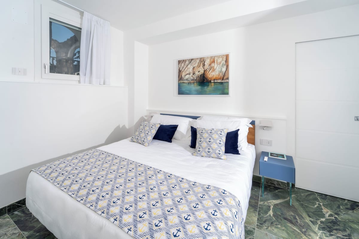 Une chambre à coucher bien rangée, avec un lit, des oreillers, une table de chevet et un tableau accroché au mur.