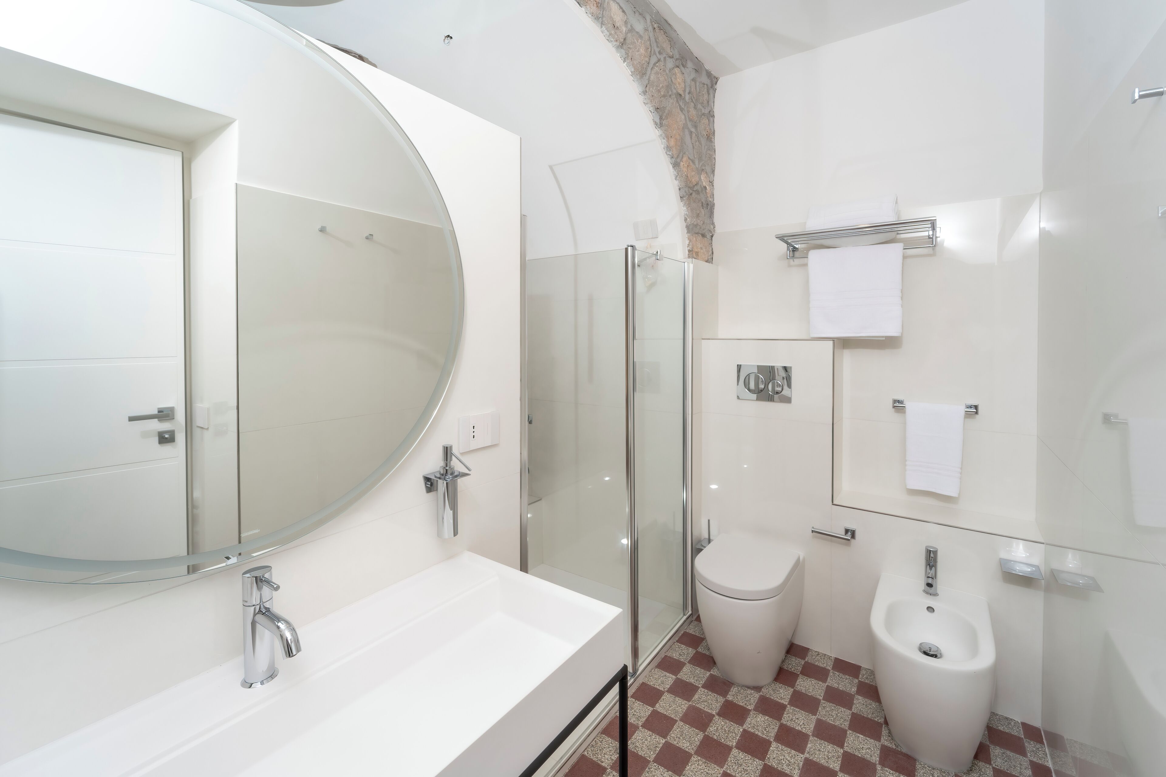 Une salle de bain moderne avec un grand miroir ovale, une baignoire sur pieds, une douche à parois de verre, des toilettes et un bidet.
