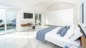 A modern bedroom with a large bed, a desk, and a view of the ocean. - Villa L'Ara (Capri)