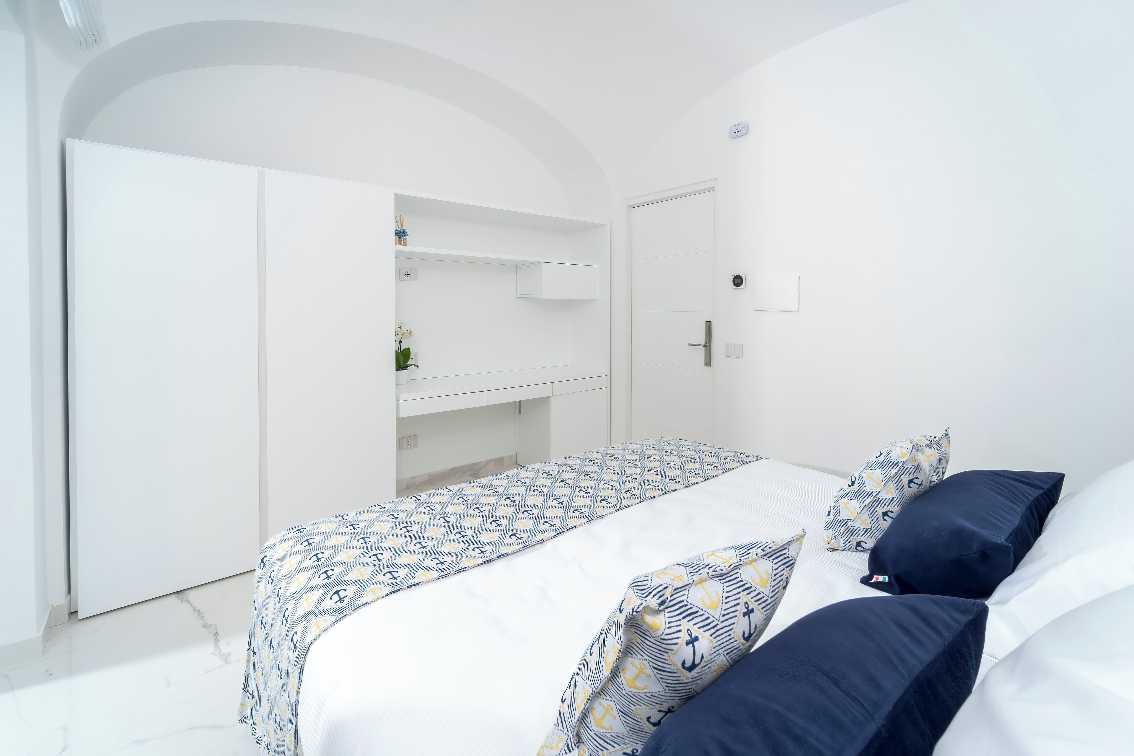 Een slaapkamer met een bed, witte muren, een witte garderobe en een witte deur.