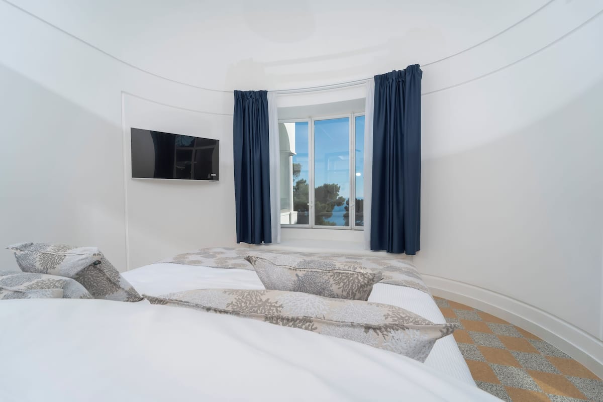 Une chambre à coucher avec un lit, un téléviseur fixé au mur et une fenêtre avec des rideaux.