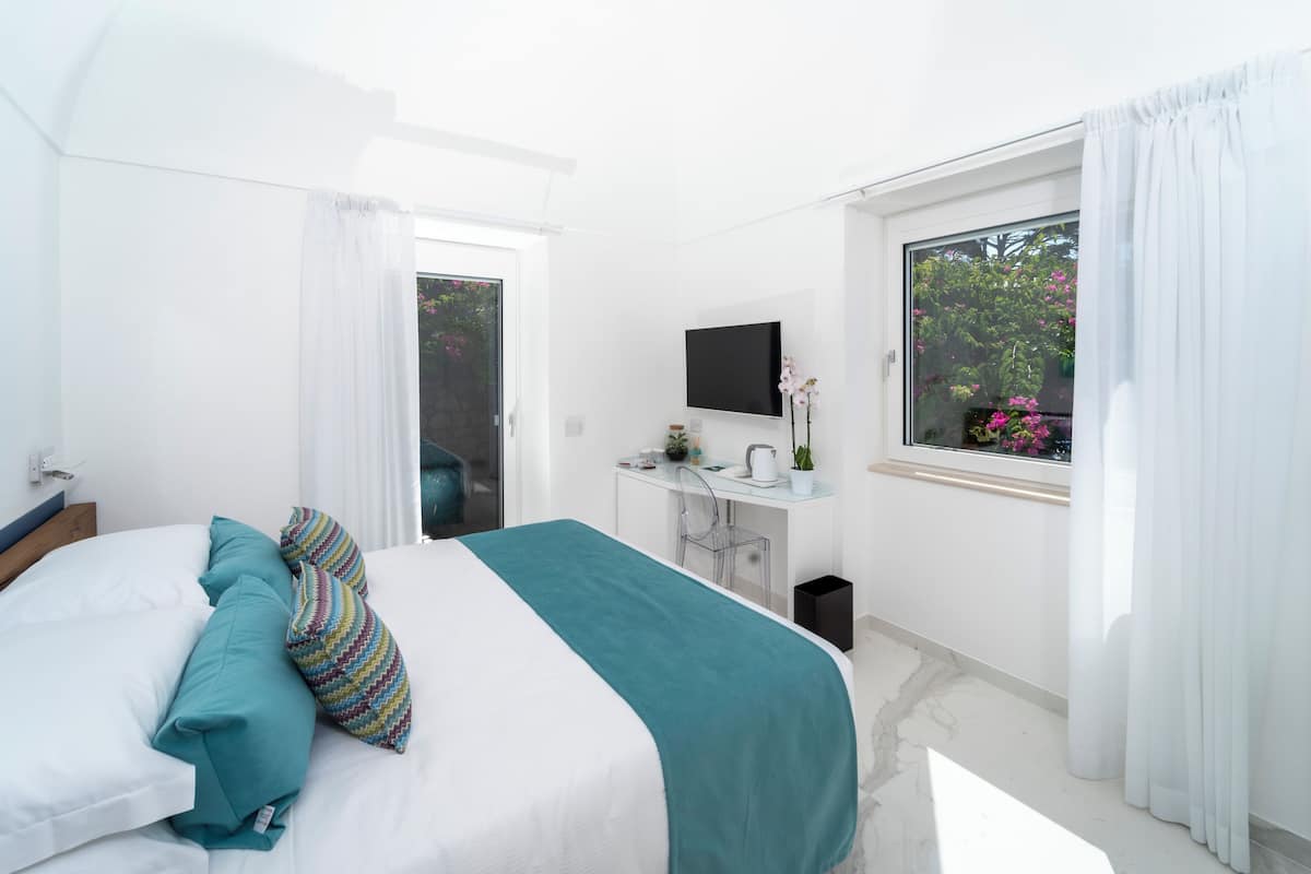Une chambre à coucher avec un lit, un bureau, une télévision et une fenêtre avec des rideaux.