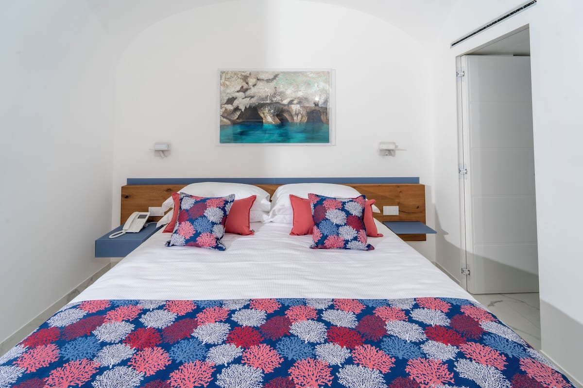 Une chambre à coucher avec un lit, deux oreillers, une table de chevet, une commode, un tableau au mur et une porte.
