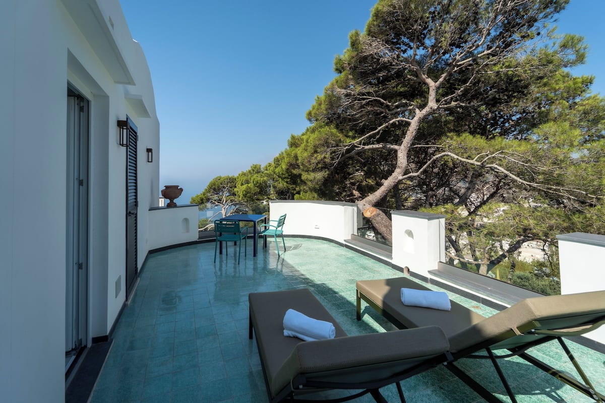 Un espace piscine aménagé sur le toit, avec des chaises longues et une table, entouré d’arbres et d’un bâtiment blanc.