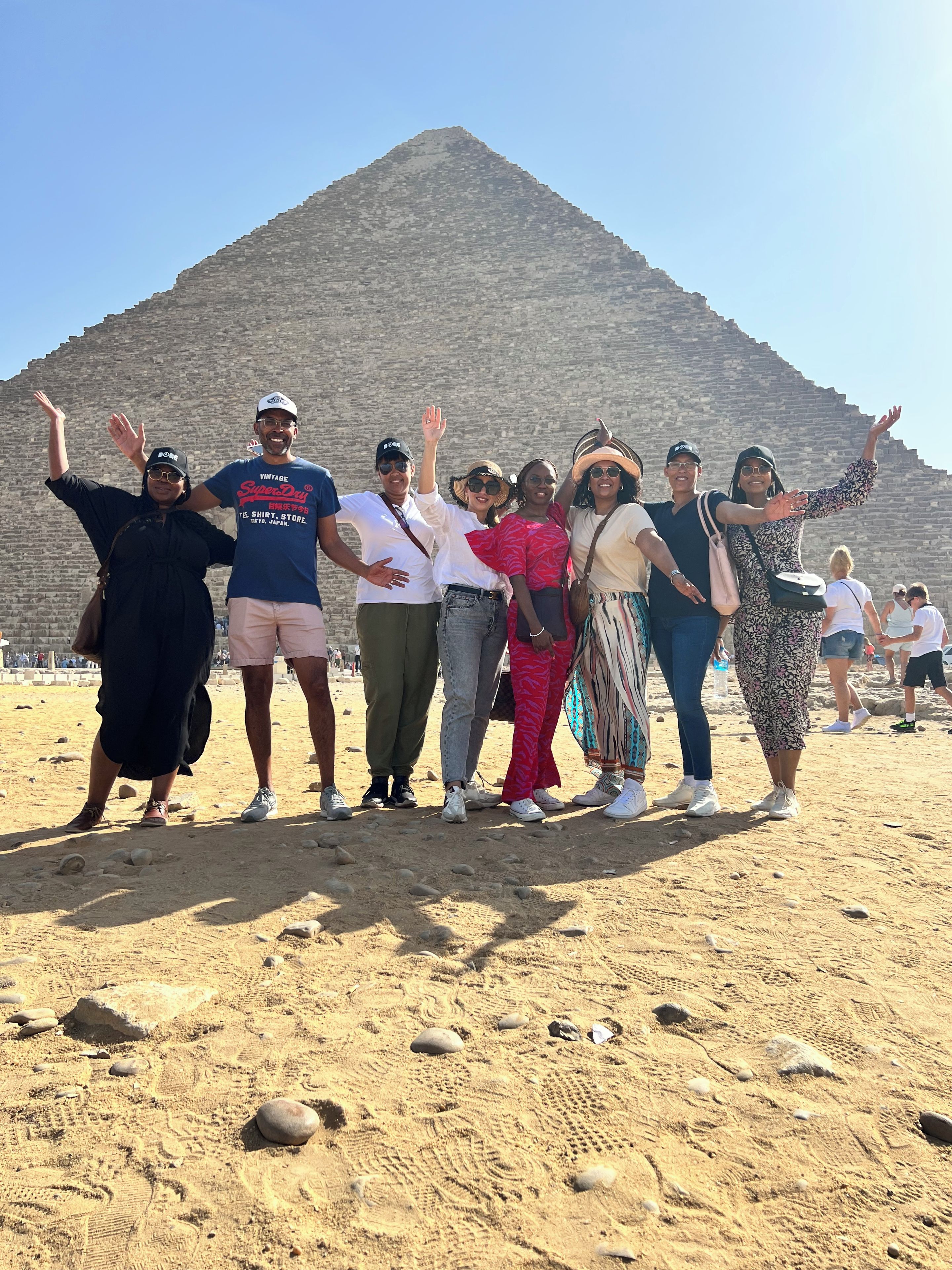 A group of people standing in a sandy area with a pyramid in the background.
