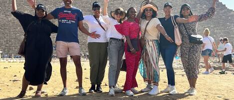 A group of people standing in a sandy area with a pyramid in the background.