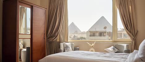 Quarto de hotel com uma cama, um guarda-roupa, dois poltronas e vista para as pirâmides.