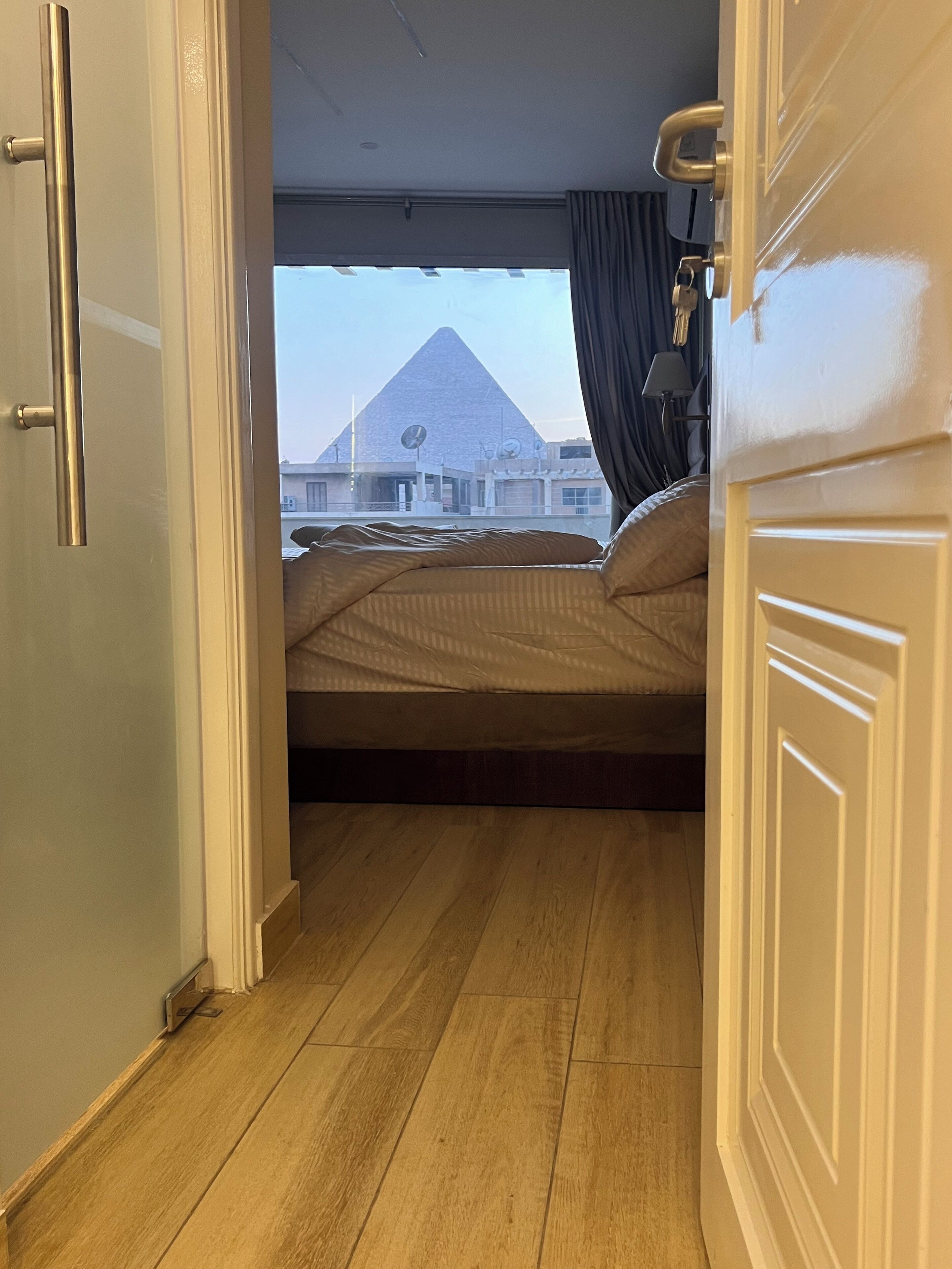 Une chambre avec un lit, un plancher en bois, une vue sur une pyramide et une porte fermée à clé.