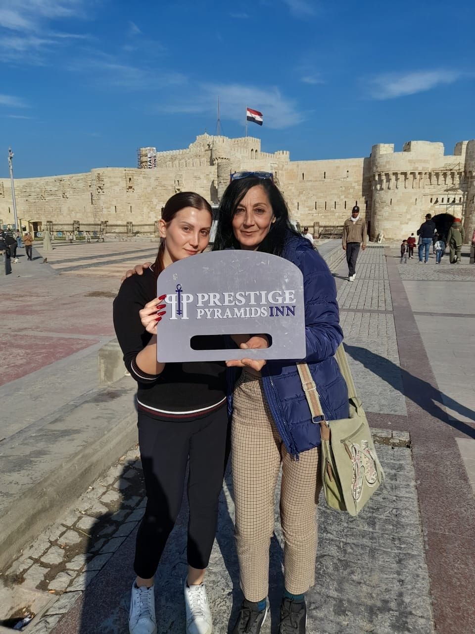 Two individuals holding a sign in front of a historic building with a flag.