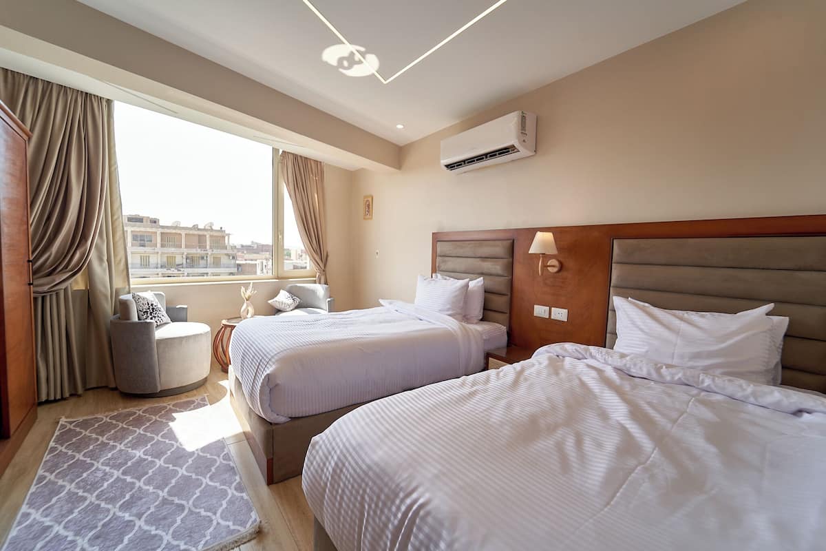 A hotel room with two beds, a sitting area, and a view of buildings.