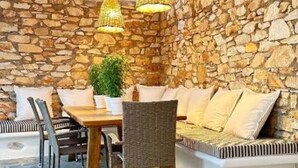 Habitació de parets de pedra amb taula i cadires de fusta, un sofà i lluminàries penjants.