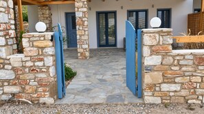 A stone pathway leading to a house with a blue door and a stone wall on the left.