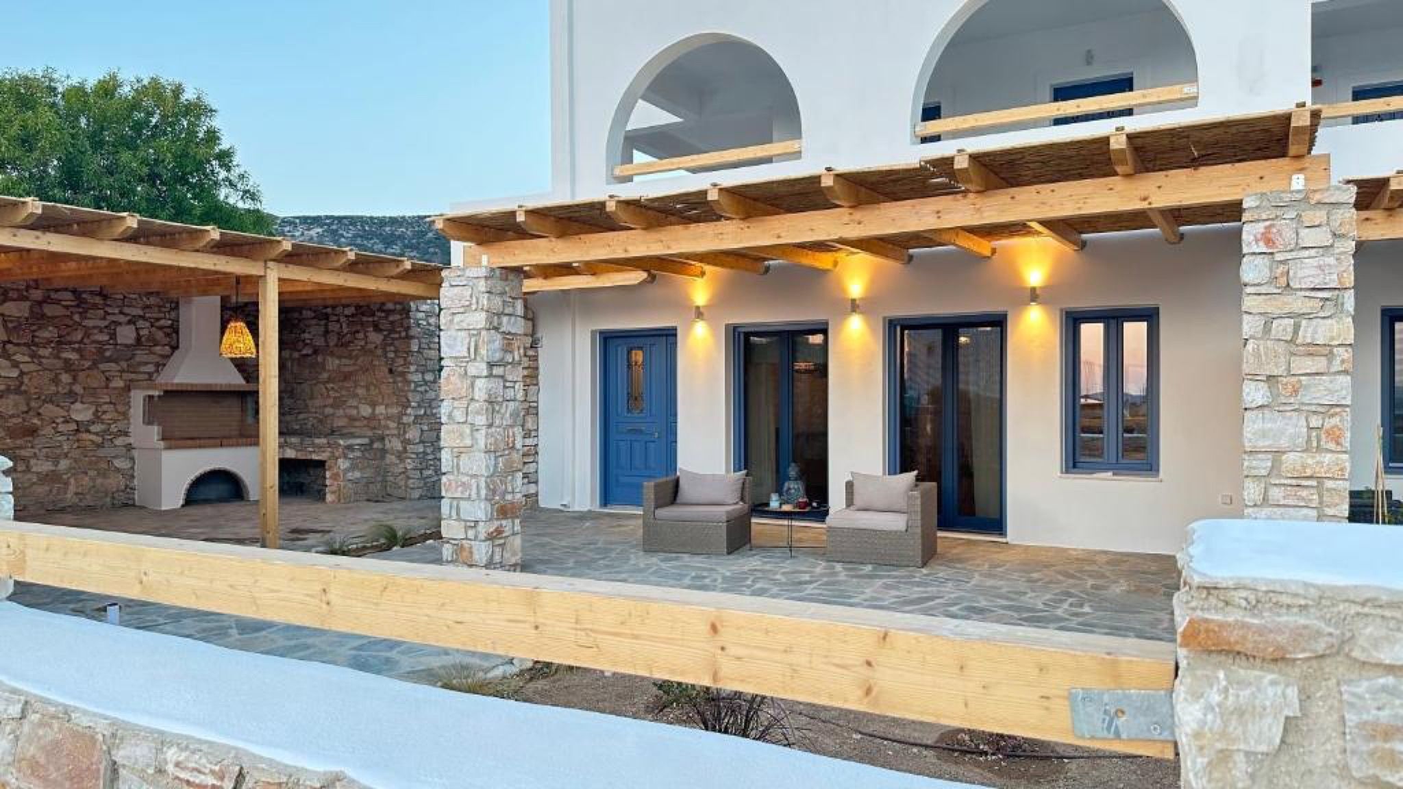 A stone building with a covered patio, outdoor seating, and a stone fireplace.