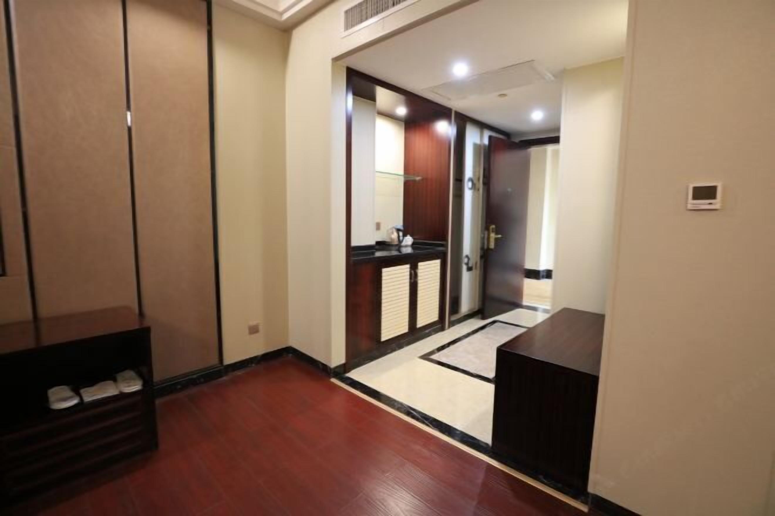A hotel hallway with a wooden floor, a shoe rack, and a door leading to a room with a black countertop and a mirror.