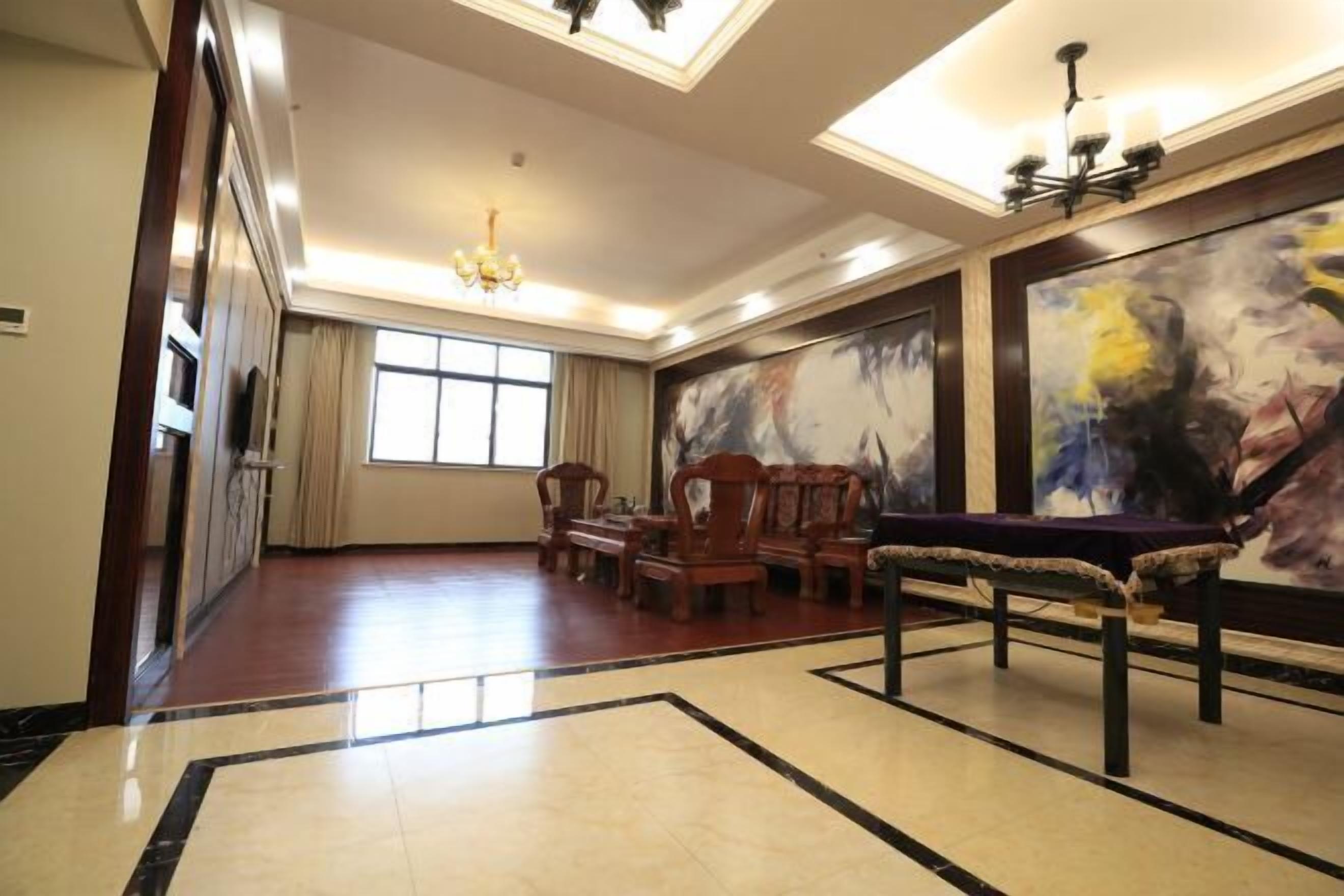A spacious room with a large painting, a chandelier, and a dining area with wooden furniture.