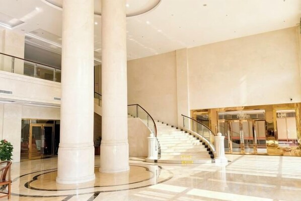 A spacious lobby with a grand staircase, large columns, and a high ceiling.