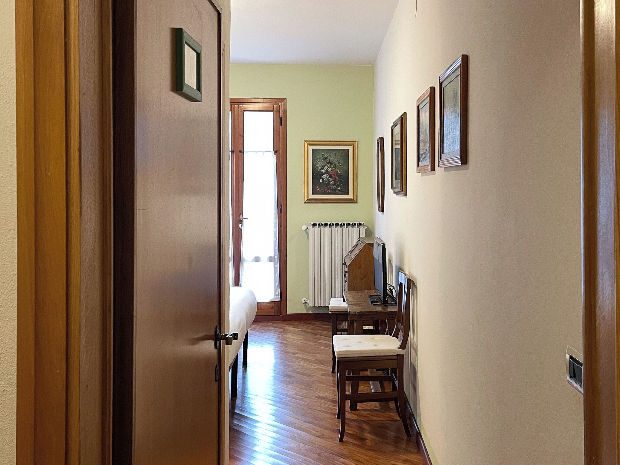 Un pasillo con suelo de madera, un radiador y cuadros enmarcados en las paredes.