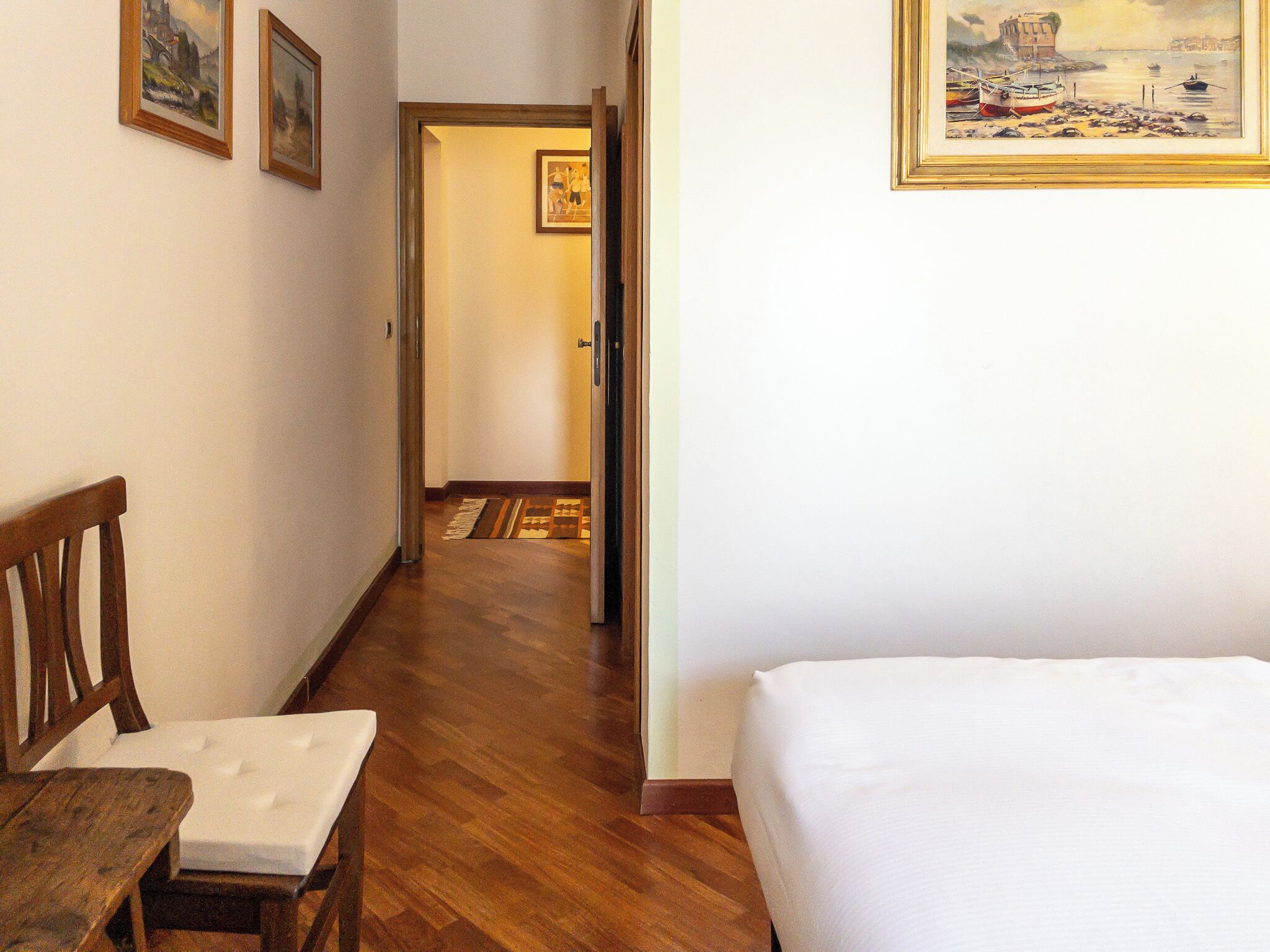 Une chambre d’hôtel avec un plancher en bois, un lit, une chaise et un couloir menant à une autre pièce.