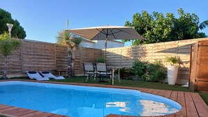 A backyard with a swimming pool, wooden deck, lounge chairs, a table, and an umbrella. - Villa 110m2 Avec Piscine Très Bonne Emplacement 10mn à Pied Plages et Commerces (Mèze)