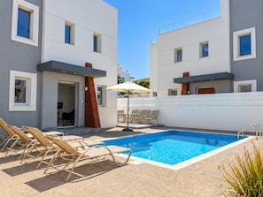 A modern building with a swimming pool, lounge chairs, and outdoor seating.