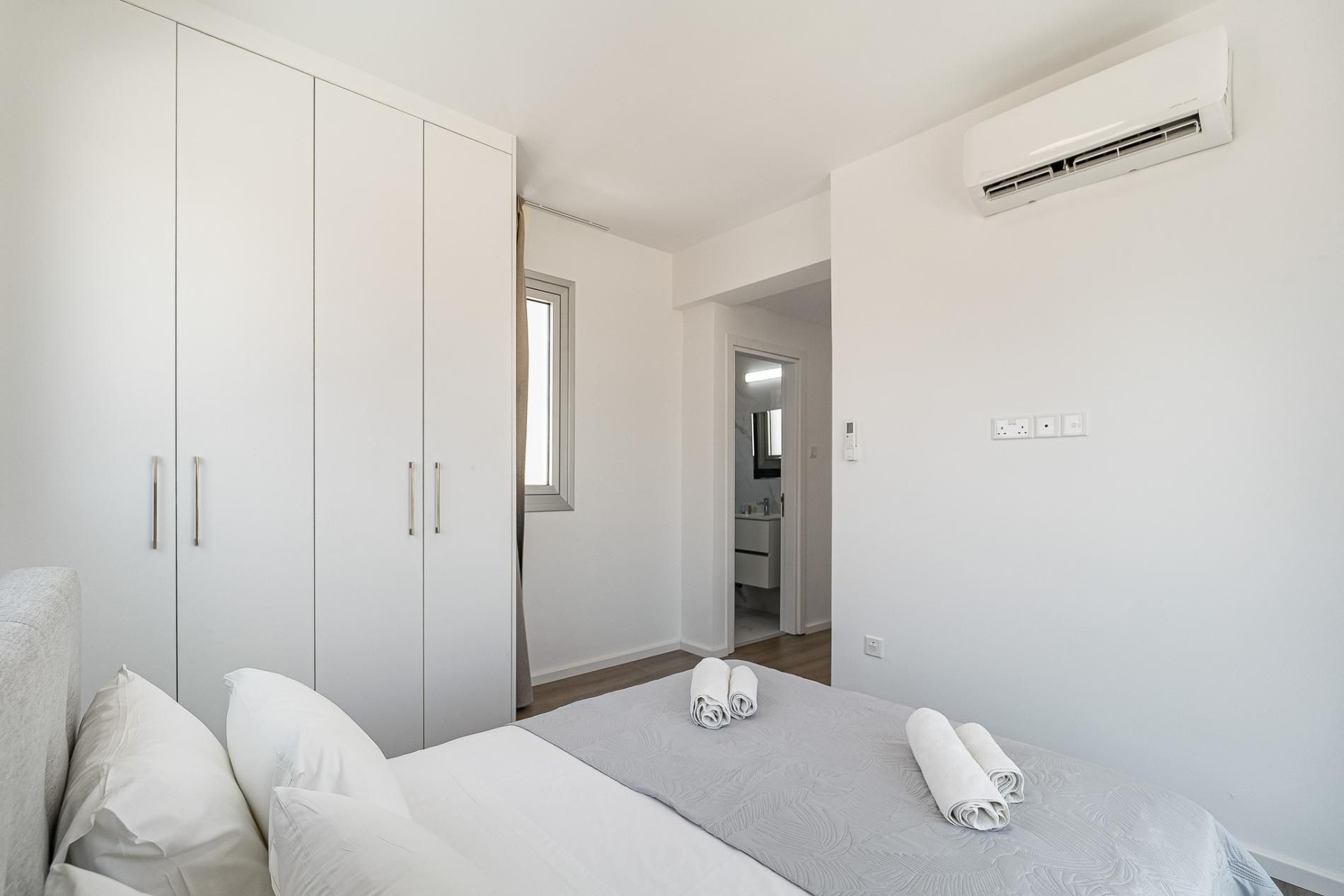 A bedroom with a bed, a wardrobe, an air conditioning unit, and a bathroom visible through an open door.