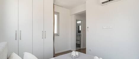 A bedroom with a bed, a wardrobe, an air conditioning unit, and a bathroom visible through an open door.