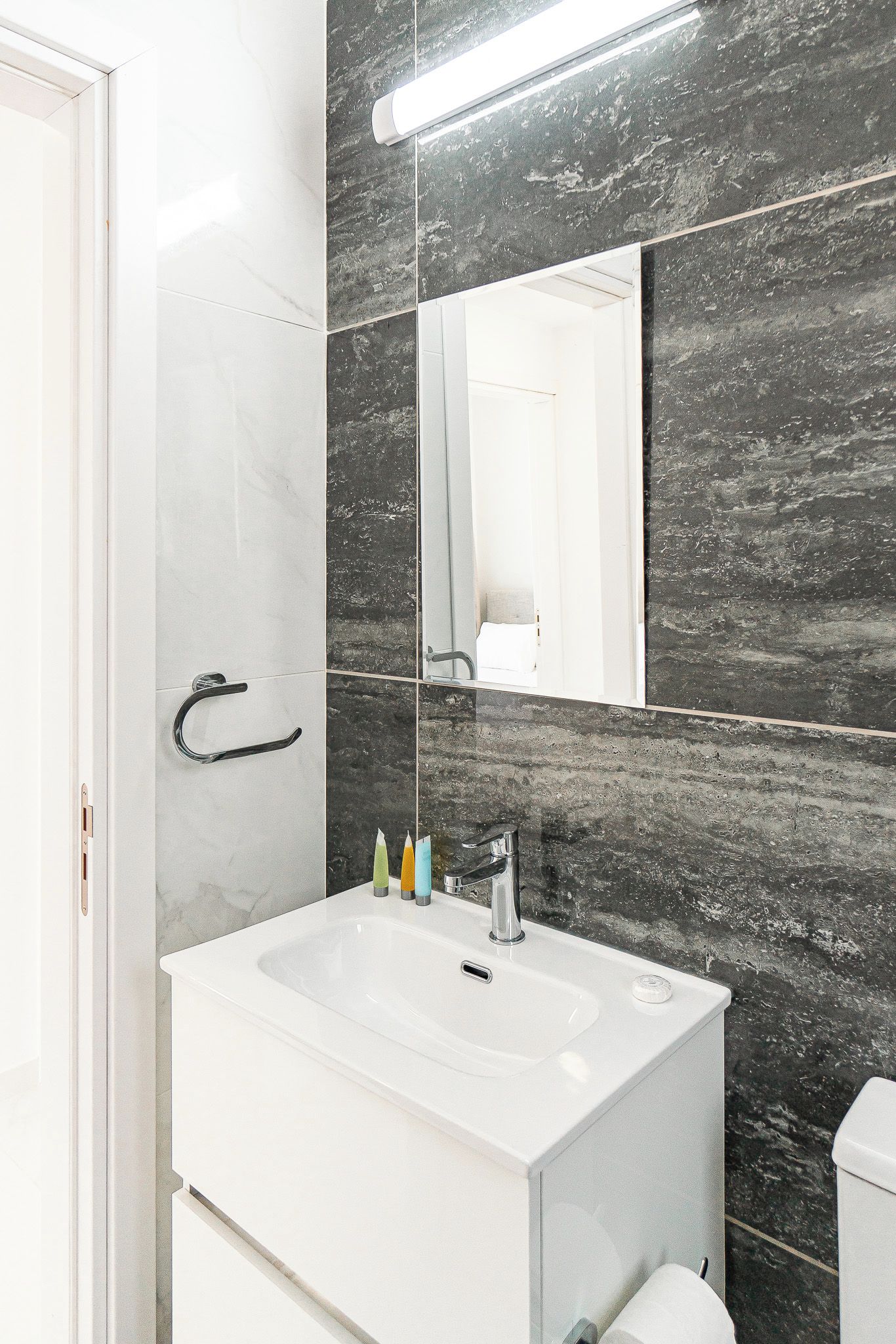 Un baño moderno con un lavamanos blanco, un espejo y una pared de mármol oscuro.