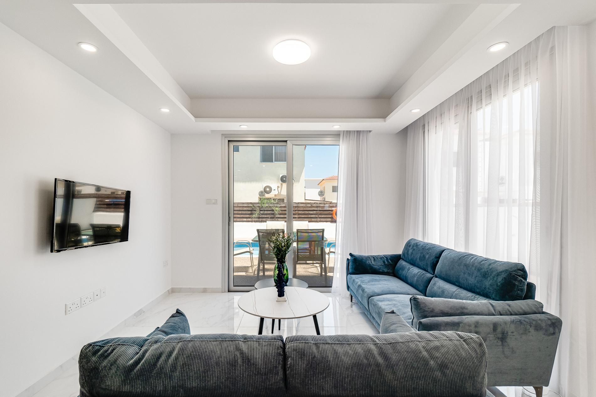 A modern living room with a sofa, a coffee table, and a flat-screen TV mounted on the wall.