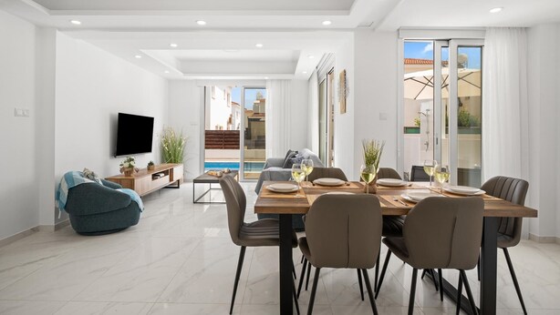 A modern dining area with a large table set for six, a sofa, and a TV mounted on the wall.