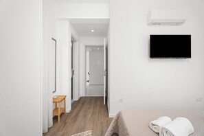 Hotellihuone, jossa on sänky, televisio, puinen yöpöytä ja käytävä, joka johtaa kylpyhuoneeseen.