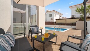 An outdoor patio with a pool, seating, and a table with drinks.