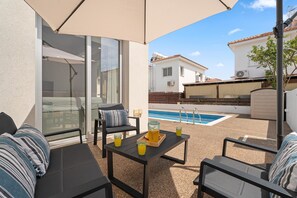An outdoor patio with a pool, seating, and a table with drinks.