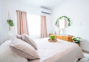A bedroom with a bed, curtains, a mirror, a dresser, and a potted plant.