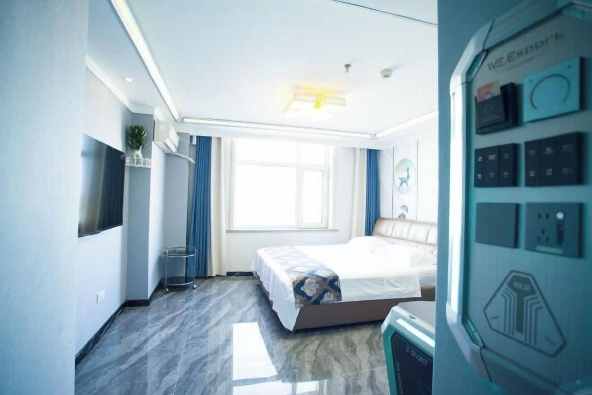 Een moderne hotelkamer met een bed, een televisie, een raam en een bedieningspaneel aan de muur.