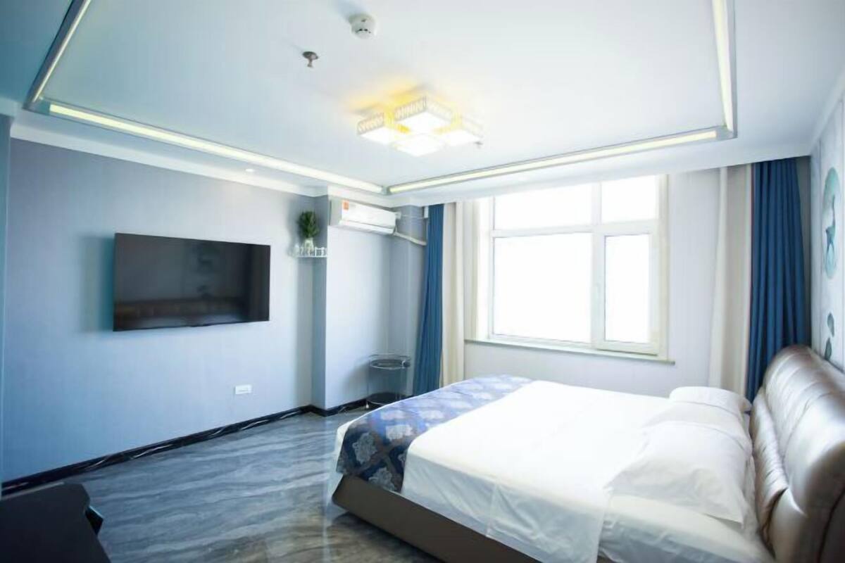 Een moderne hotelkamer met een bed, een flatscreen-tv, een airconditioner en een raam met gordijnen.