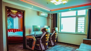 Een hotelkamer met een bed, massagestoelen, een bureau met een computer en een groot raam.