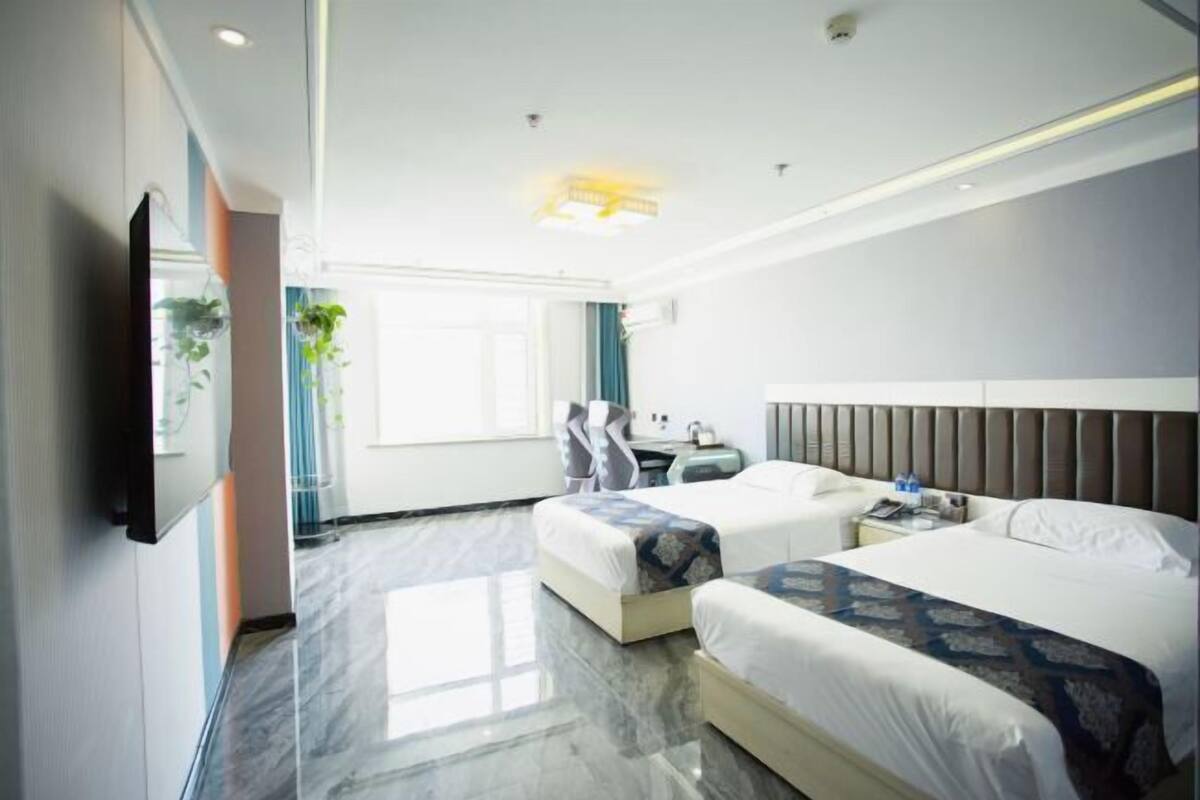Een hotelkamer met twee bedden, een flatscreen-tv, een bureau en een raam met gordijnen.