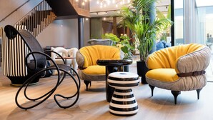 Un intérieur moderne avec un escalier, des fauteuils jaunes, un pouf rayé et une chaise noire.