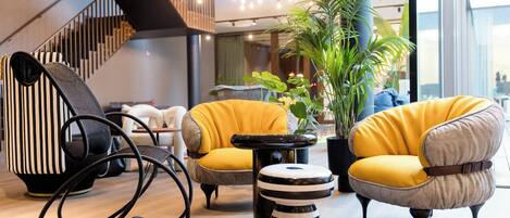 A modern interior with a staircase, yellow armchairs, a striped ottoman, and a black chair.