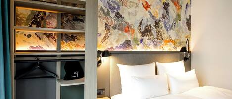 A hotel room with a bed, a wardrobe, and a colorful abstract painting on the wall.